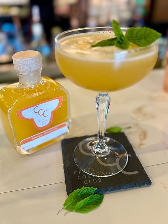 picture of a orange drink in a margarita glass next to a bottle on cream tiles in a bar setting