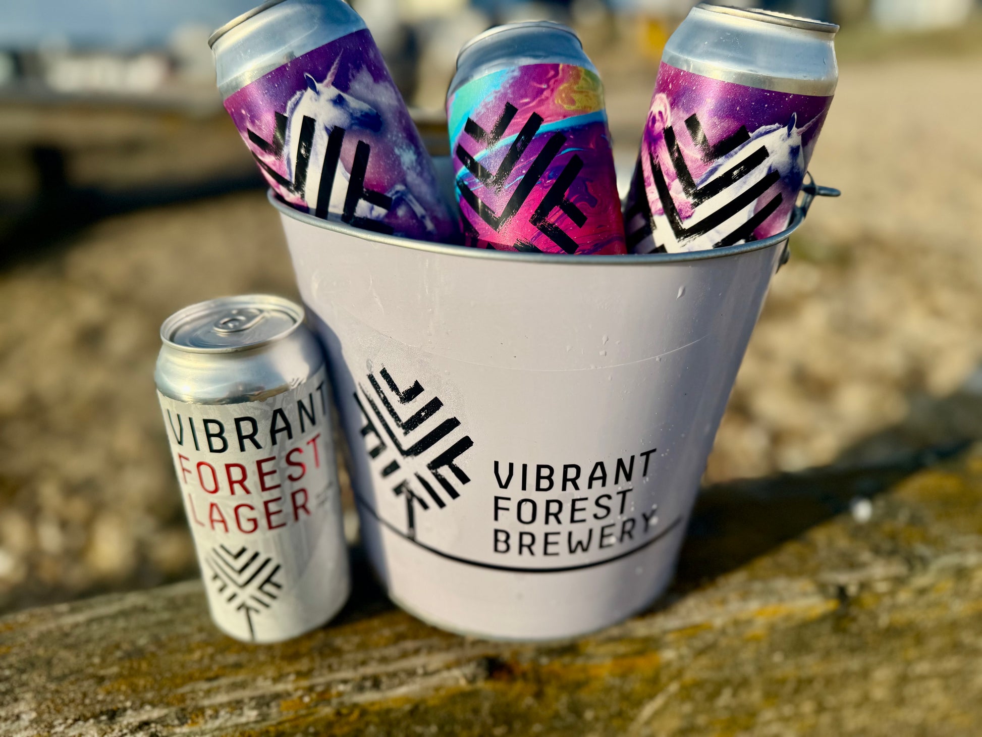 Colorful beer cans in a bucket with 'Vibrant Forest Brewery' branding on a wooden surface.