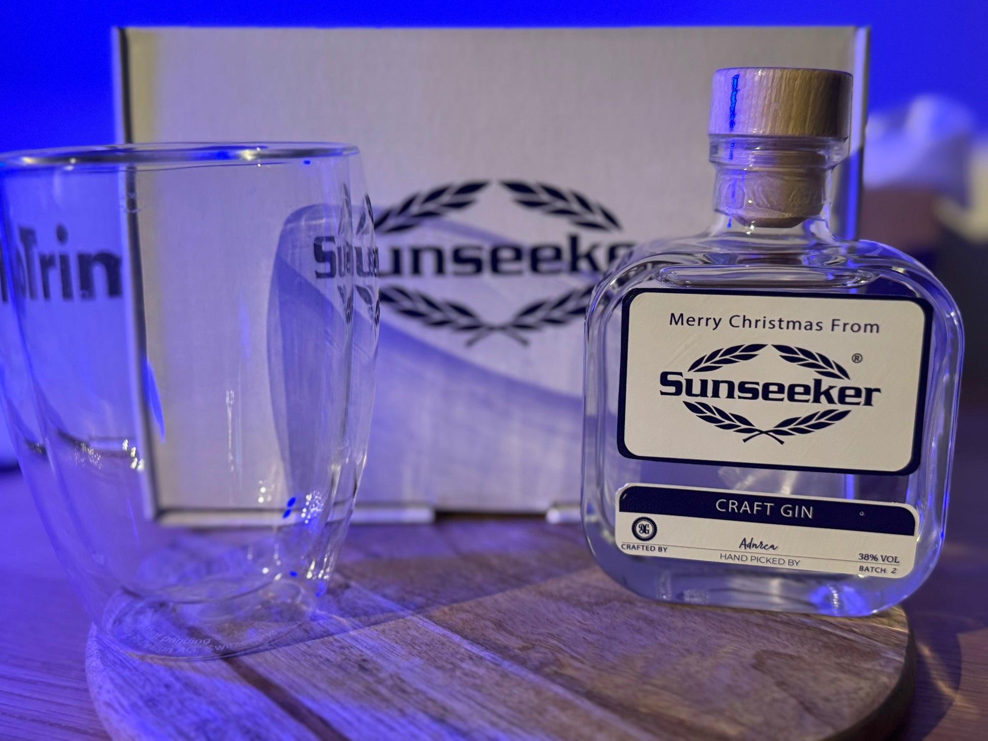 Sunseeker craft gin bottle with a glass on a wooden surface, branded Corporate gift box in the background.