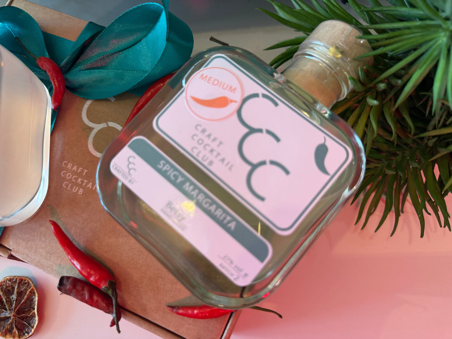 Picture of  Craft cocktail bottle of spicy margarita, the bottle is square glass and is surrounded by Chillies  