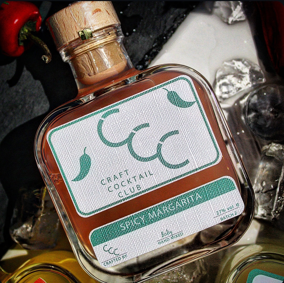 Bottle of Spicy Margarita from Craft Cocktail Club with ice cubes and a red pepper in the background