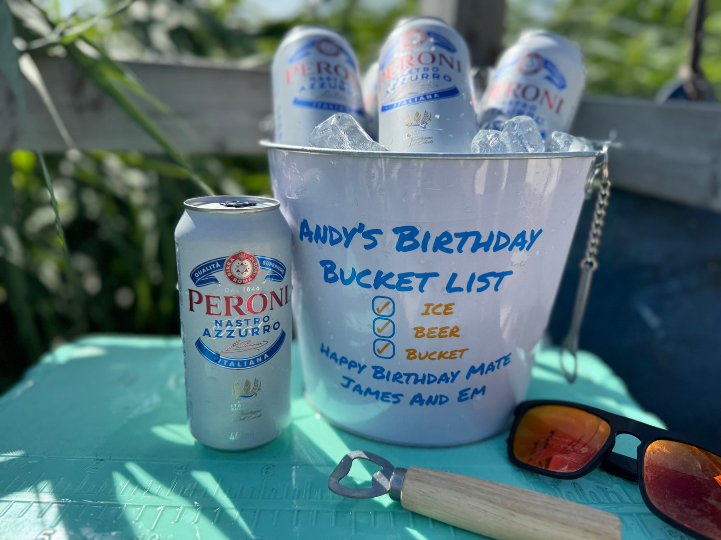 A beer bucket sat on a cooler, with 4 beers and ice inside on the bucket is a personalised message saying happy birthday