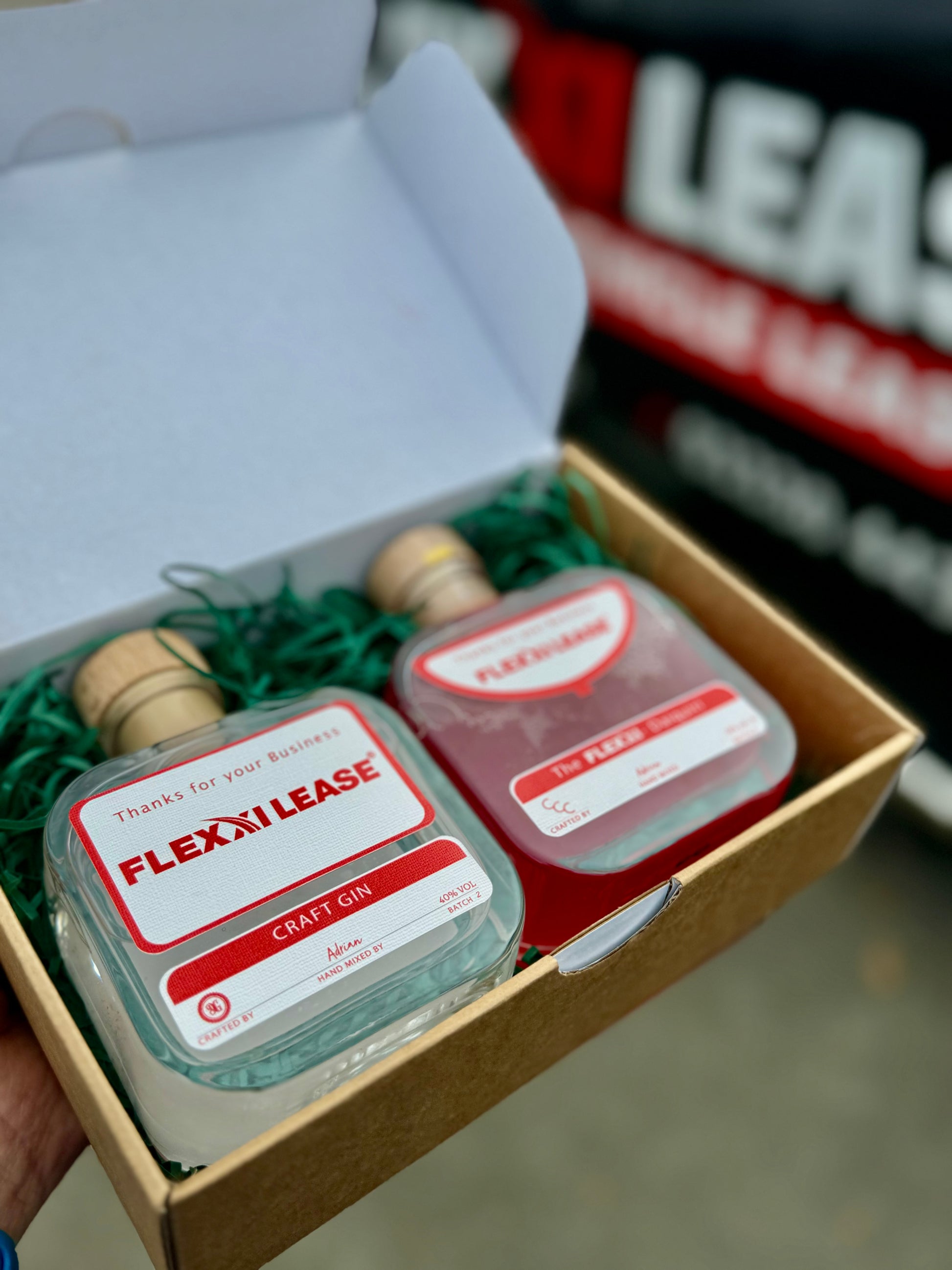 Two small bottles labeled 'Flexi Lease' in a box with greenery, blurred background. Corporate gift box 